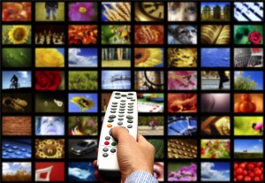 hand holding a remote control against a wall of multiple screens for digital television